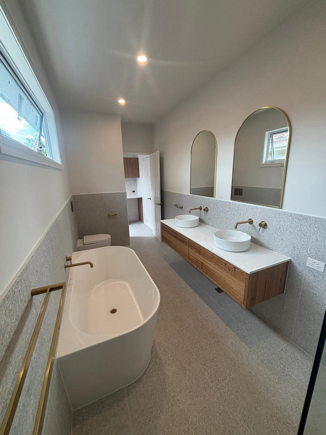 Renovated main bathroom with freestanding bath, floating timber double vanity, twin arched mirrors and brass tapware