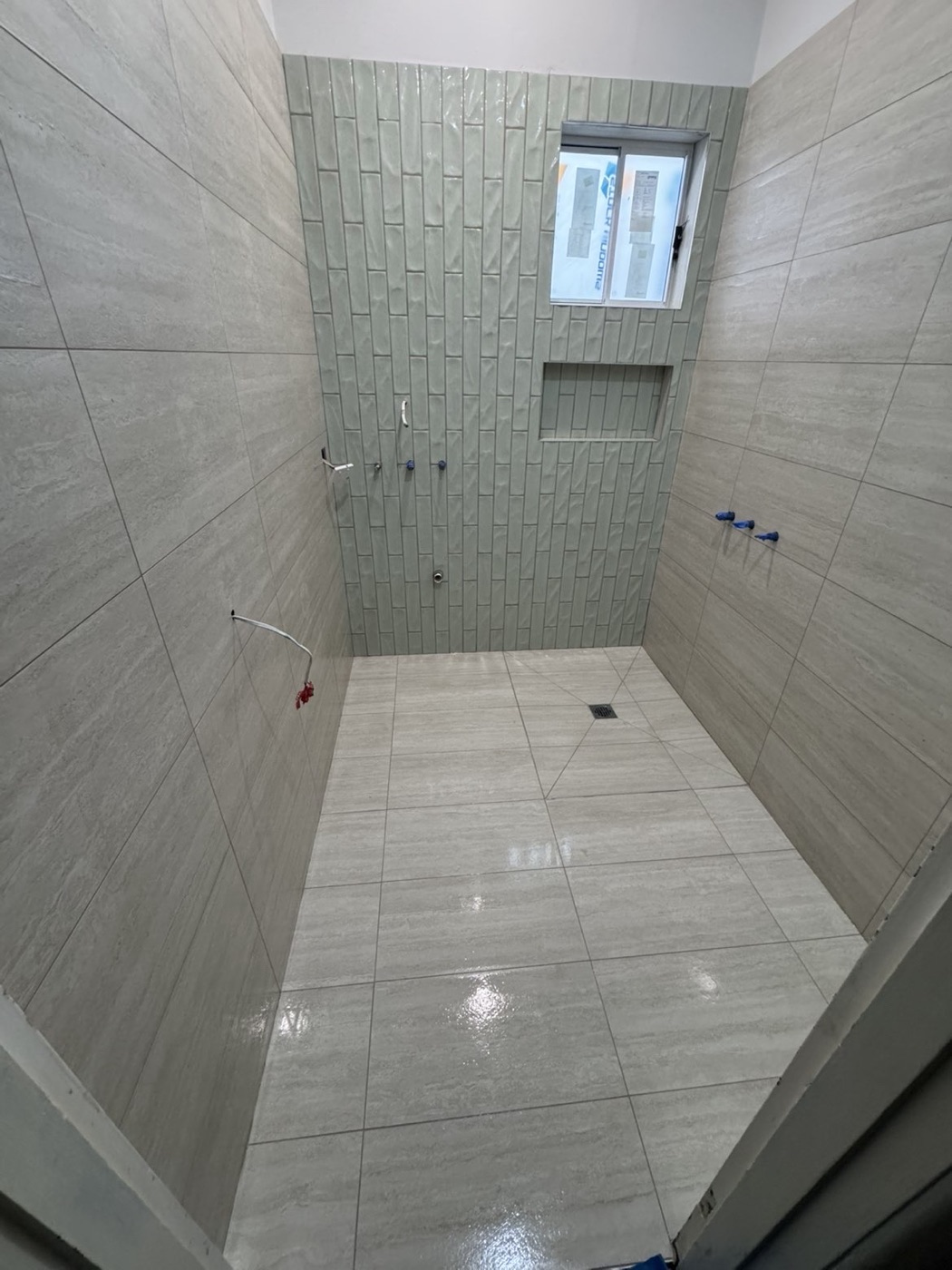 Bathroom shower fully tiled in stone with a sage-green feature wall and recessed niche